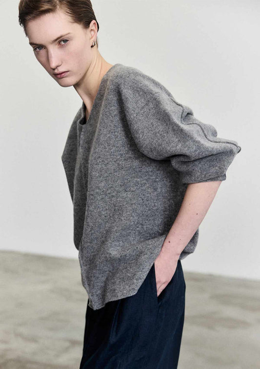 Side view of model wearing the relaxed fitting grey merino sweater with a V-neckline and coat sleeves by Leophil