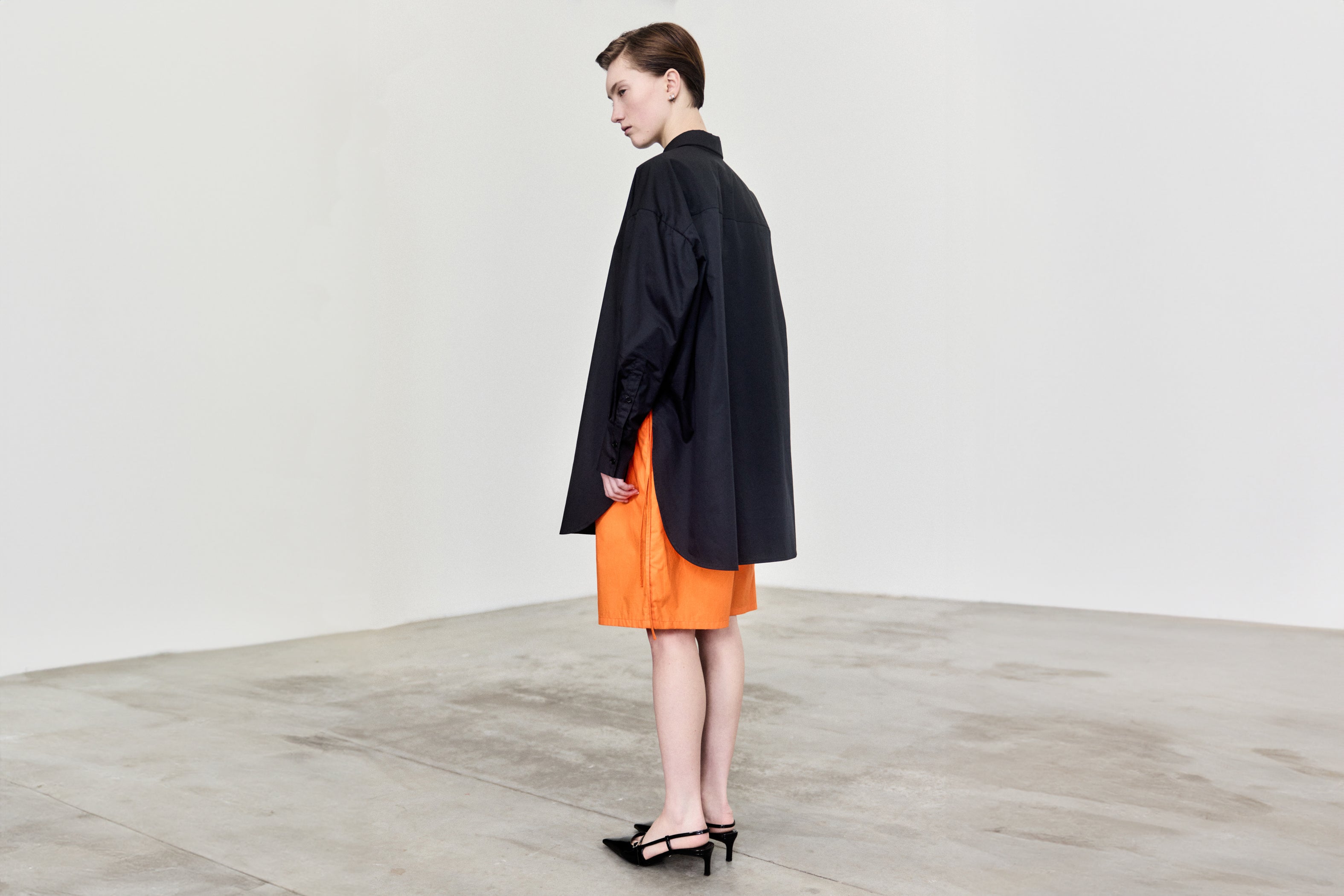 Woman wearing the new TRISTAN Extra Wide Poplin Shirt in black over the ERNST Shorts in bright orange